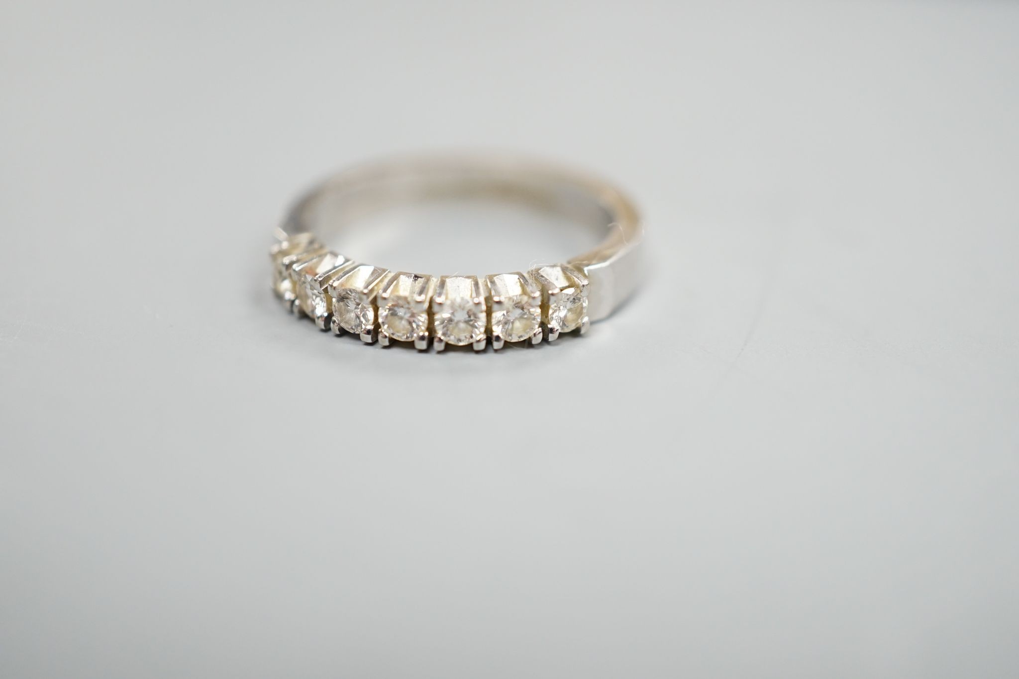 A modern 18k white metal and seven stone diamond set half eternity ring, size M, gross weight 4.4. grams.
